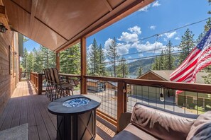 Une terrasse en bois avec un foyer, des sièges d’extérieur et une vue sur un paysage montagneux.