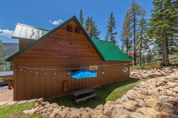Une cabane en bois avec un toit vert, une petite piscine et une table de pique-nique.