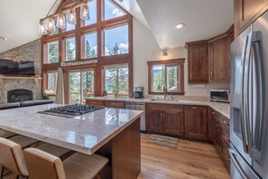 A spacious kitchen with a large island, wooden cabinets, and a stone fireplace. - Donner Lakeview Home for 10 Private Hot-Tub (Truckee)