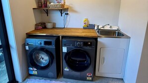 Une petite buanderie équipée de deux machines à laver à chargement frontal, d’un évier et d’étagères en bois au-dessus.