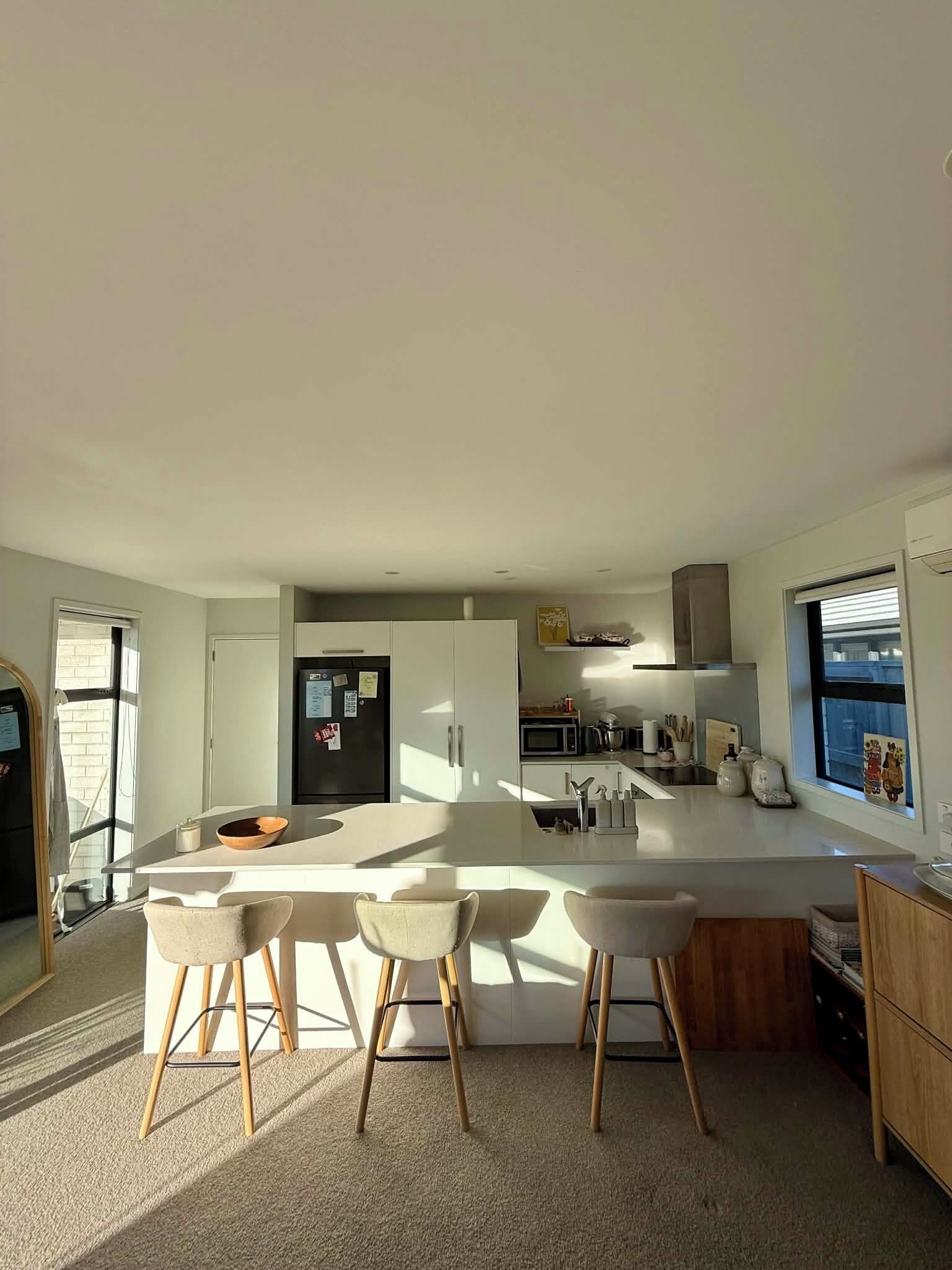 A modern kitchen with a central island, bar stools, and a microwave.