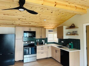 Une cuisine avec des meubles de rangement en bois, un réfrigérateur noir, une cuisinière, un four à micro-ondes et un ventilateur de plafond.