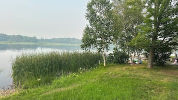 Vista para um lago, com grama, árvores e águas calmas.