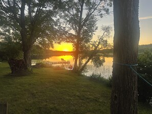 Un cadre paisible au bord du lac, avec une jetée en bois, des arbres et une vue dégagée sur le coucher de soleil sur l’eau.
