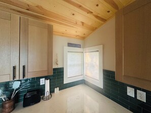 Une cuisine avec des meubles de rangement en bois, un pare-feu en carreaux verts et une fenêtre avec des stores.