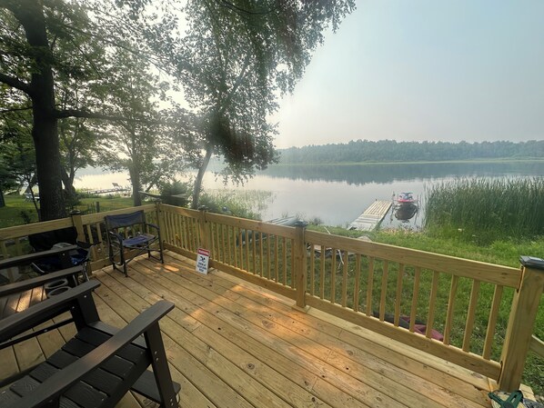 Une terrasse en bois offrant une vue sur un lac paisible, un quai et un panneau d’avertissement.