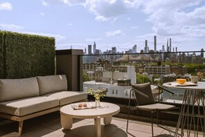 Eine Dachterrasse mit einer Sitzecke, einem Tisch und einem Sessel mit Blick auf eine Stadtlandschaft.