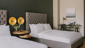 Ett hotellrum med två sängar, ett skrivbord och en stol. Det finns två runda vägglampor och en inramad tavla på väggen.