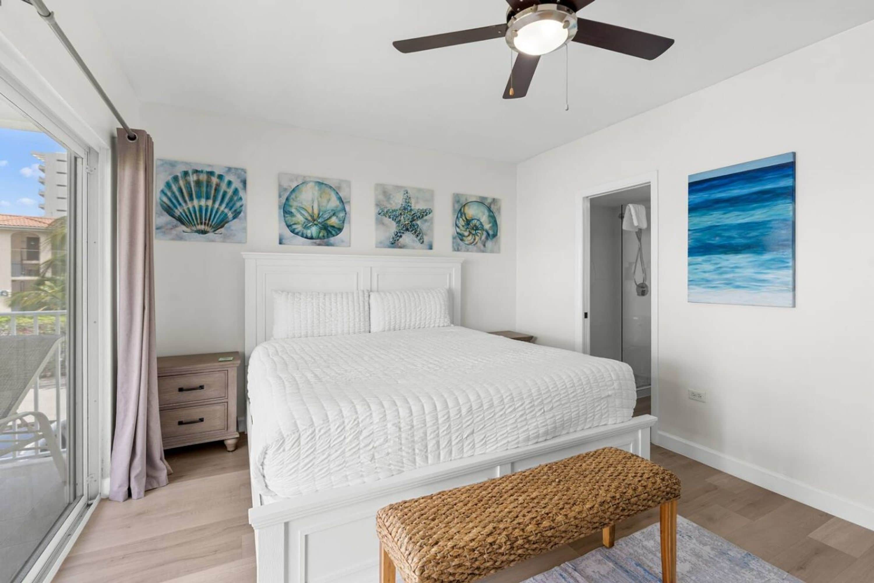 A bedroom with a bed, a ceiling fan, a bench, and artwork on the wall.