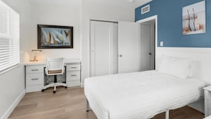 Un dormitorio con cama, escritorio, silla y un cuadro en la pared.