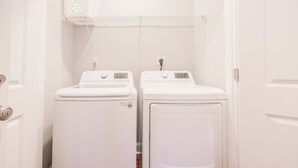 A laundry room with two white front-loading washing machines and a metal shelf above them.