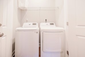 A laundry room with two white front-loading washing machines and a metal shelf above them.