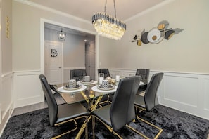 A dining room with a chandelier, black chairs with gold accents, and a patterned wall decoration.
