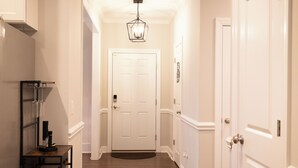 A hallway with a white door at the end, a black shelf with glasses, and a light fixture above.