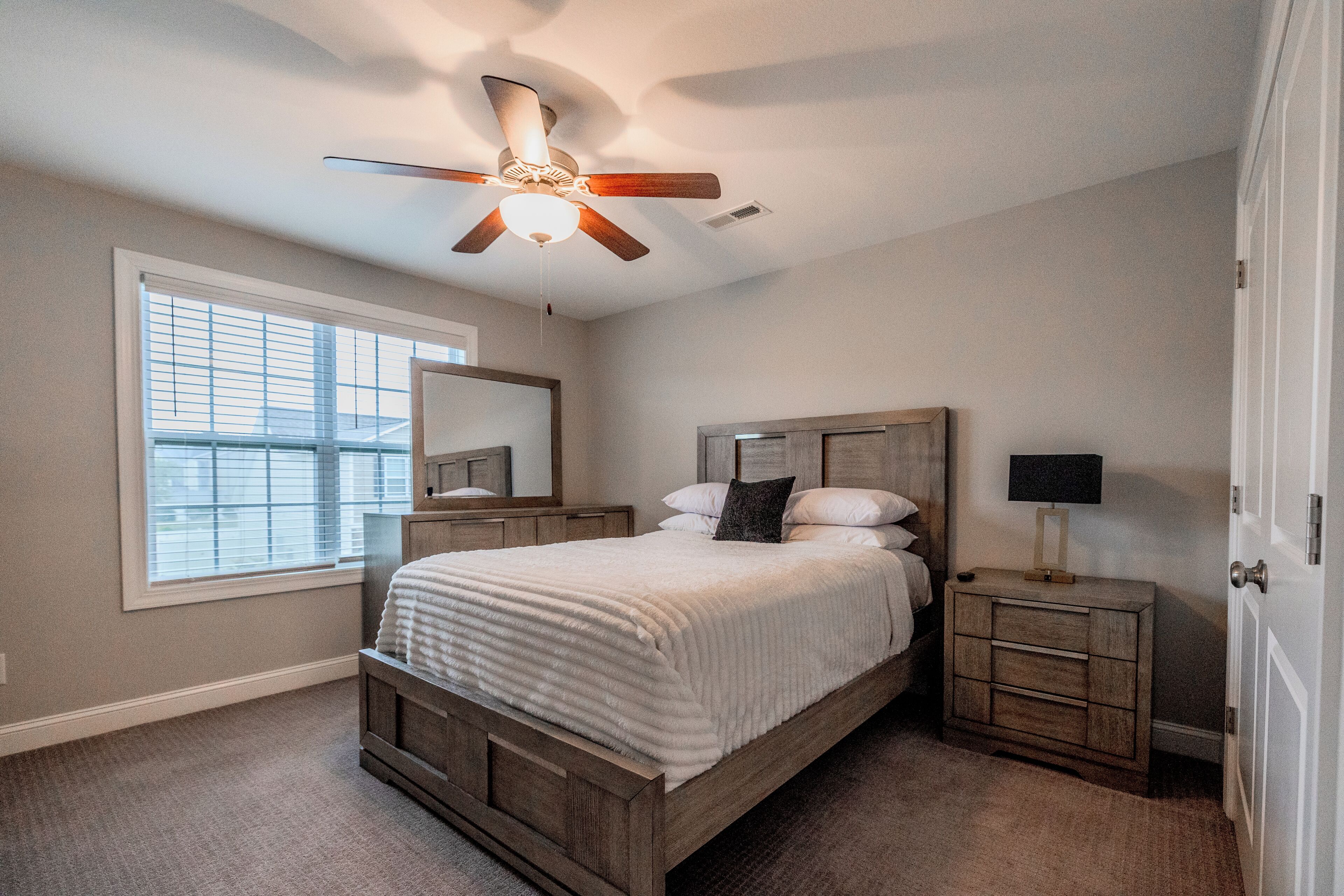 A bedroom with a bed, a nightstand, a mirror, a ceiling fan, and a window.