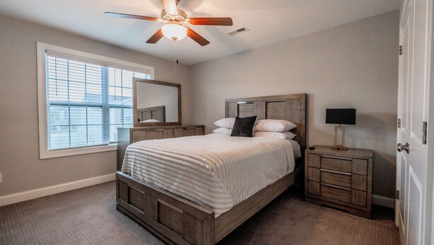 A bedroom with a bed, a nightstand, a mirror, a ceiling fan, and a window.