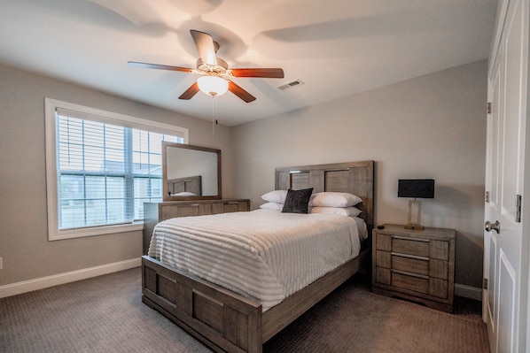 A bedroom with a bed, a nightstand, a mirror, a ceiling fan, and a window.