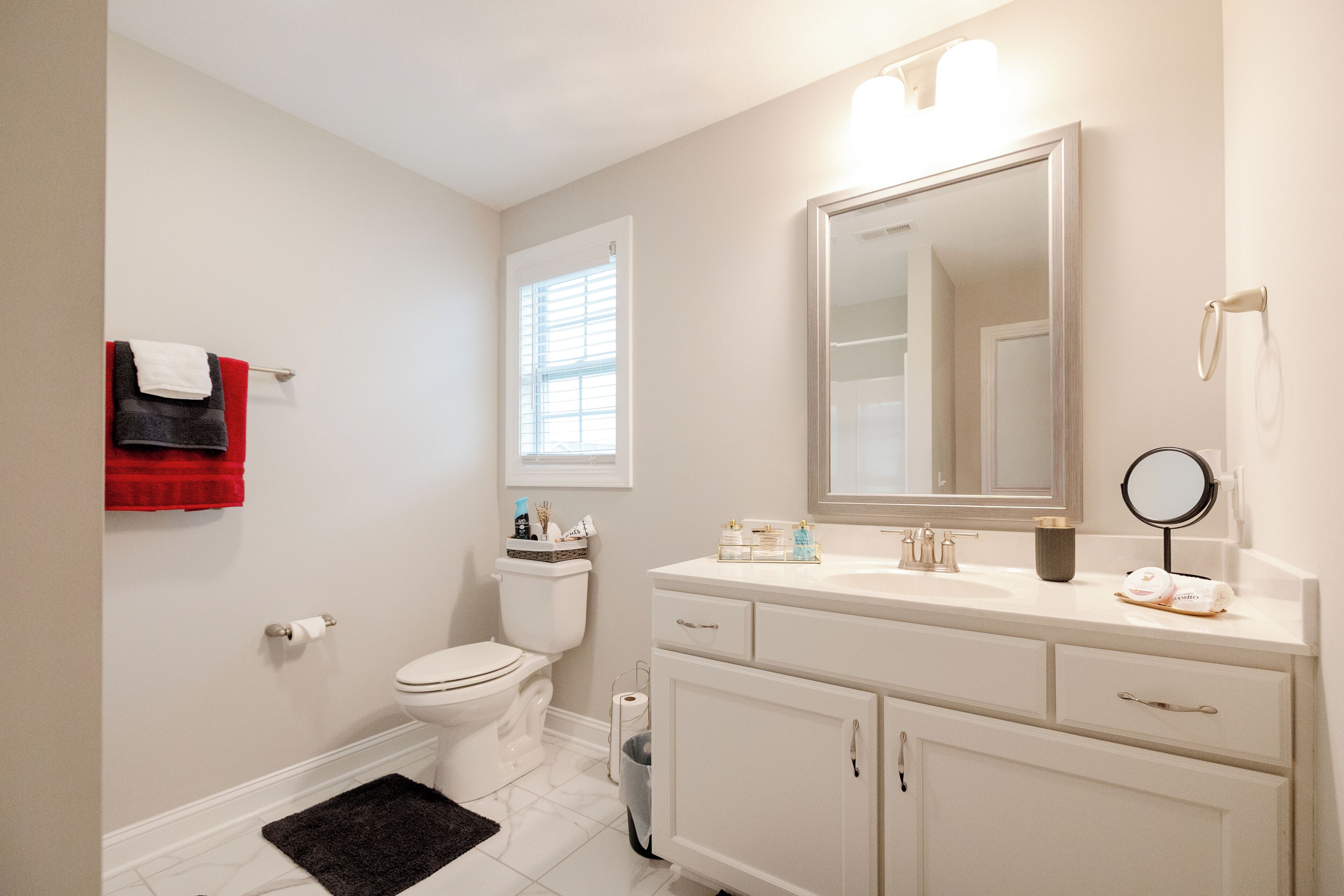 A bathroom with a toilet, sink, mirror, and a towel rack with a red towel.