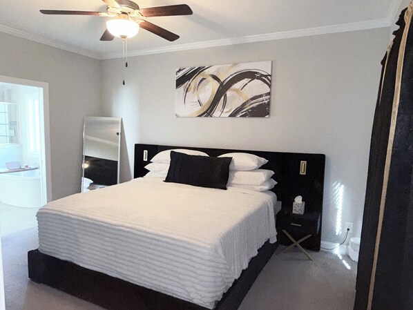A bedroom with a bed, a ceiling fan, a wall-mounted artwork, and a door.