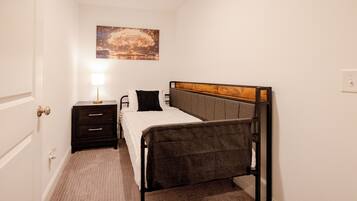 A bedroom with a single bed, a bedside table, a lamp, and a wall-mounted painting.