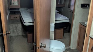 Een compact RV-interieur met twee bedden, een toilet en een kleine badkamer.