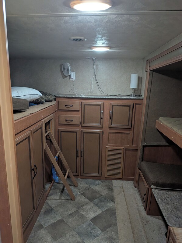 A compact kitchen with wooden cabinets, a built-in stove, and a fan on the wall.