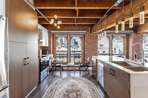 A modern kitchen with wooden cabinets, a central island, and a view of the city through large windows. - Spacious & Charming 3BR - Heart of Old Montreal (Montréal)