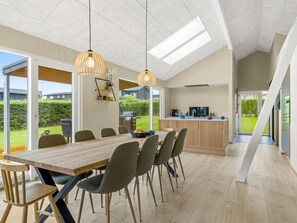 Eine moderne Küche mit einer großen Kochinsel, einem Essbereich mit Holztisch und Stühlen sowie Blick ins Freie.