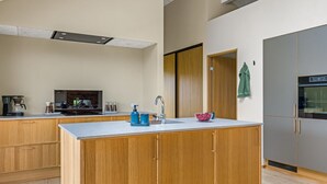 A modern kitchen with wooden cabinets, a central island, a built-in oven, and a coffee machine. - "Illona" - 200m from the sea by Interhome (Hejls)
