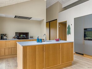 Eine moderne Küche mit Holzschränken, einer zentralen Kochinsel, einem eingebauten Backofen und einer Kaffeemaschine.