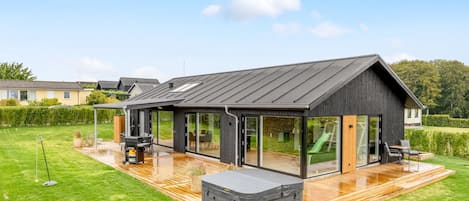 A modern house with a deck, outdoor seating, and a hot tub.