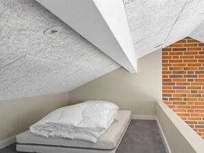Ein kleiner, kompakter Raum mit einem Einzelbett, einer Ziegelwand und einer geneigten Decke.