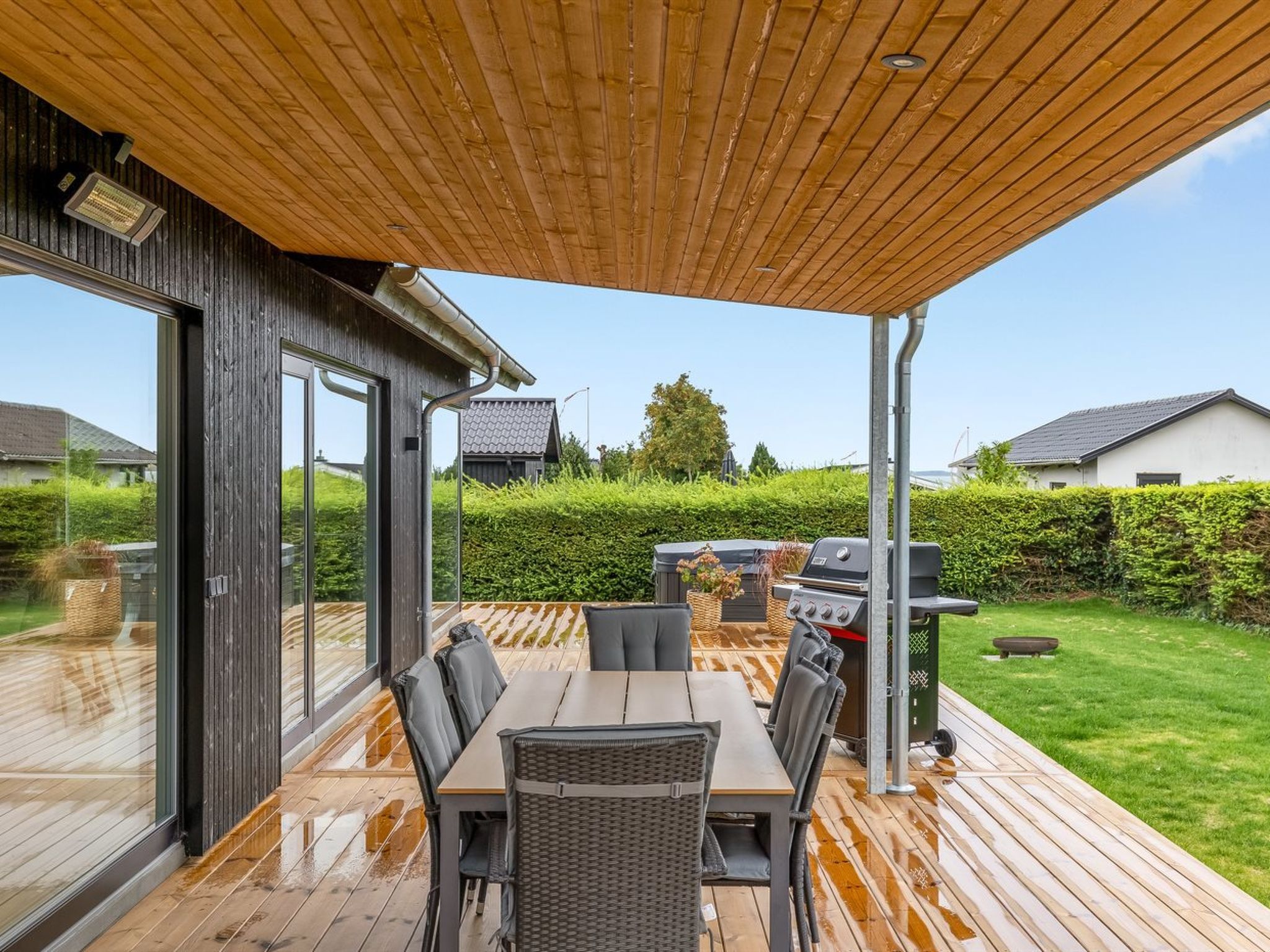 Un patio extérieur couvert avec une terrasse en bois, une table et des chaises, ainsi qu’un barbecue.