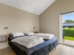Une chambre à coucher avec un lit, des tables de chevet et une vue sur un jardin, accessible par une porte coulissante.