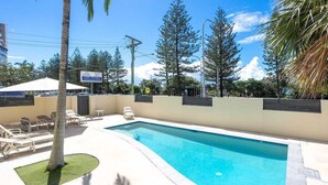 A swimming pool with lounge chairs, a palm tree, and a sign indicating a hotel. - Wyuna Ocean Views in Burleigh (Gold Coast)