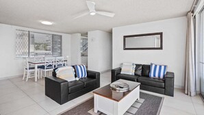 A modern living room with two black sofas, a coffee table, and a dining area with a white table and chairs. - Wyuna Ocean Views in Burleigh (Gold Coast)
