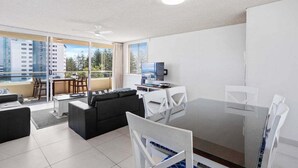 A modern living room with a glass dining table, black sofa, and white chairs. - Wyuna Ocean Views in Burleigh (Gold Coast)