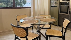 A dining area with a round table and four chairs, a refrigerator, and an oven in the background.