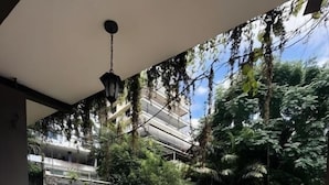 A balcony with a table set for breakfast, a railing, and a view of a garden and building.