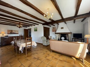 Ein rustikales Wohnzimmer mit freiliegenden Holzbalken, einem Kamin, einem Esstisch mit Stühlen und einem Sofa.