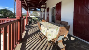 A covered outdoor seating area with a table and chairs, a view of the mountains, and a red railing. - MENDIKO-LOREA - SAINT-PEE-SUR-NIVELLE (SAINT-PEE-SUR-NIVELLE)