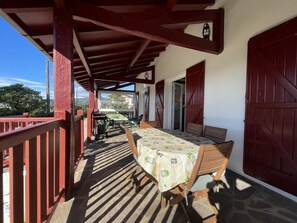 A covered outdoor seating area with a table and chairs, a view of the mountains, and a red railing. - MENDIKO-LOREA - SAINT-PEE-SUR-NIVELLE (SAINT-PEE-SUR-NIVELLE)