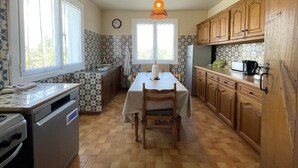A kitchen with a dining table, wooden cabinets, a stove, and a clock on the wall. - MENDIKO-LOREA - SAINT-PEE-SUR-NIVELLE (SAINT-PEE-SUR-NIVELLE)