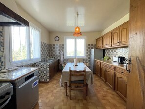 A kitchen with a dining table, wooden cabinets, a stove, and a clock on the wall. - MENDIKO-LOREA - SAINT-PEE-SUR-NIVELLE (SAINT-PEE-SUR-NIVELLE)