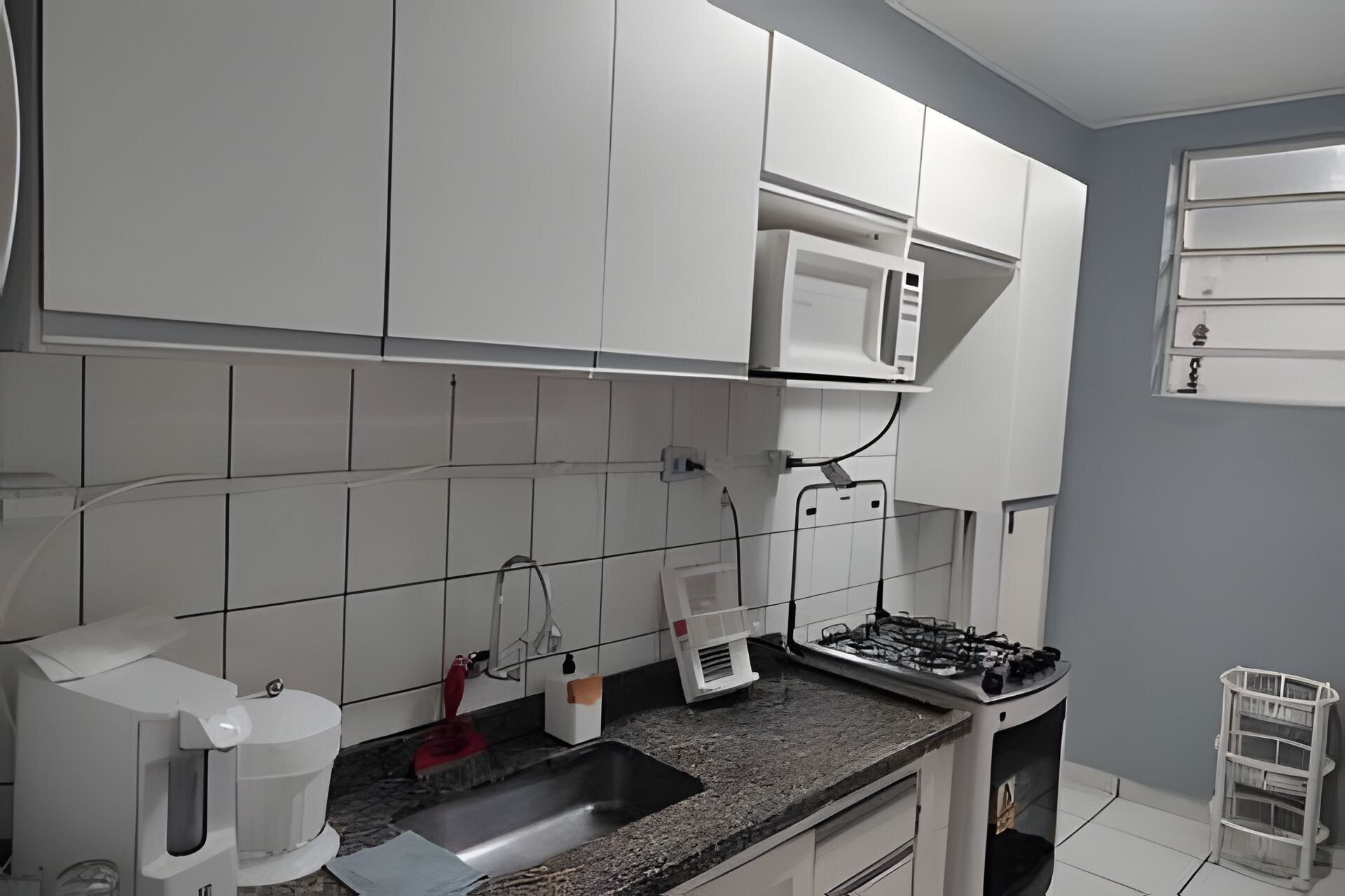 A kitchen with white cabinets, a microwave, a gas stove, a coffee maker, and a sink.