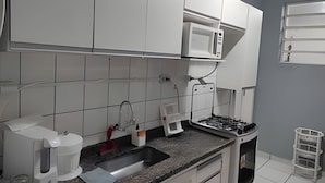 A kitchen with white cabinets, a microwave, a gas stove, a coffee maker, and a sink. - Quarto Quádruplo Augusta Paulista e Frei (São Paulo)