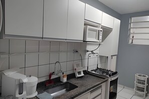 Eine Küche mit weißen Schränken, einer Mikrowelle, einem Gasherd, einer Kaffeemaschine und einem Spülbecken.