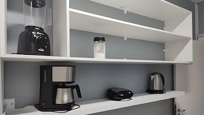 A kitchenette with a coffee maker, a kettle, and a water bottle on a white shelf. - Quarto Quádruplo Augusta Paulista e Frei (São Paulo)