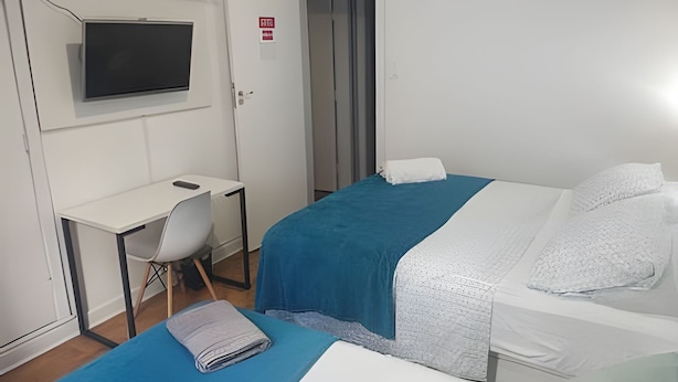 A hotel room with a bed, a desk, a chair, and a television. - Quarto Quádruplo Augusta Paulista e Frei (São Paulo)