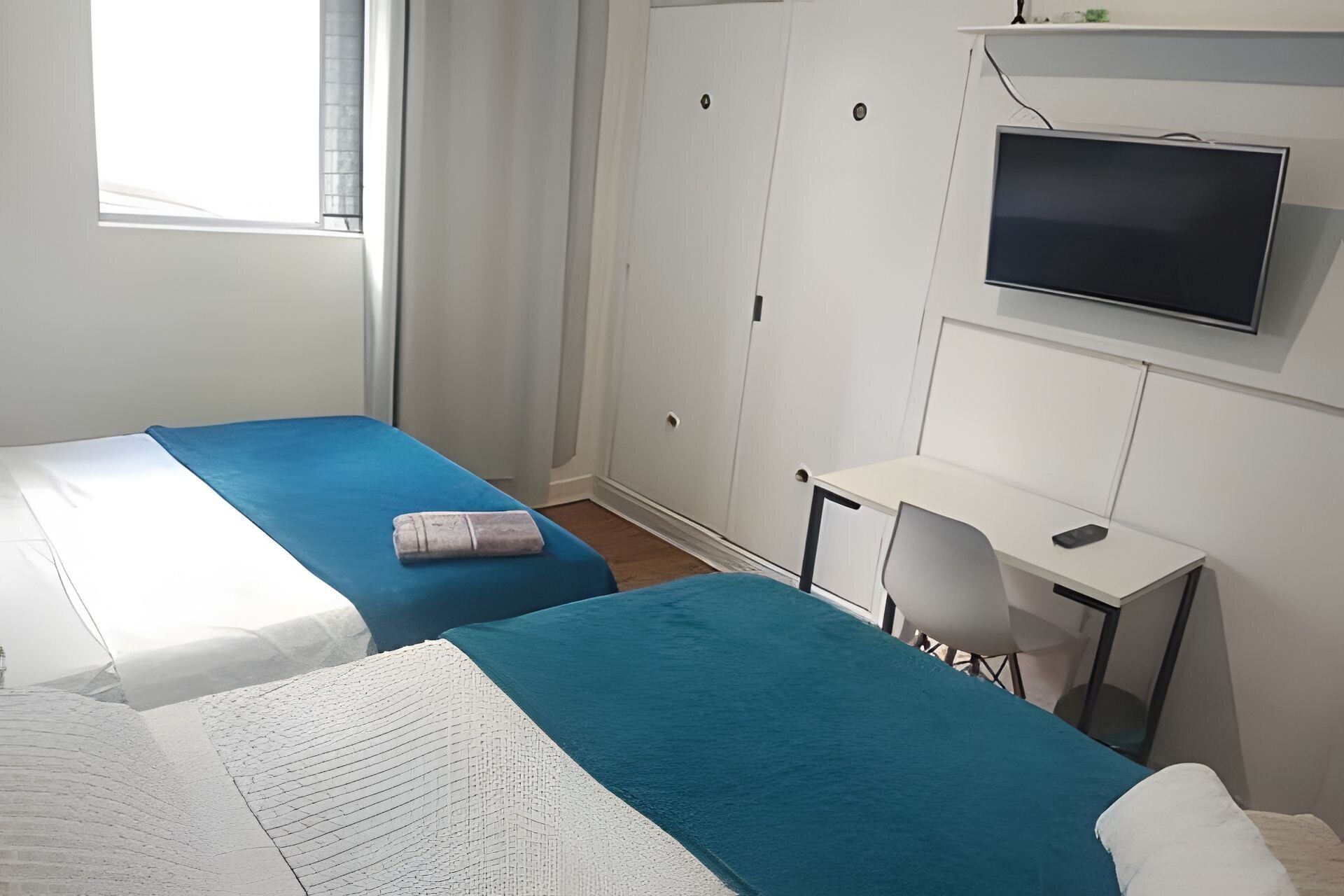 A room with two beds, a desk, a chair, and a television.
